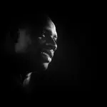Omar Sy souriant lors d’une avant-première en 2014, photographie d’archive en noir et blanc.
