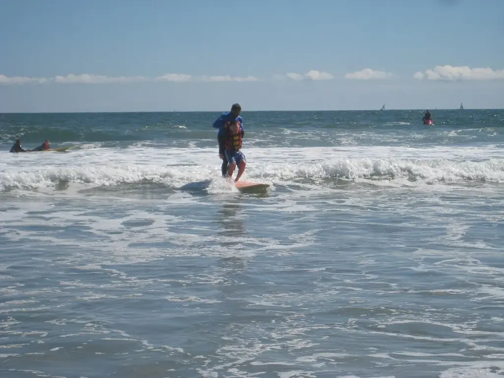 Un enfant et un adulte en combinaison sur une planche lors d’une séance de surf adapté