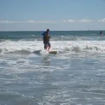 Un enfant et un adulte en combinaison sur une planche lors d’une séance de surf adapté