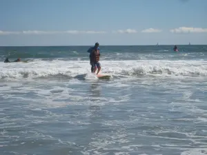 Un enfant et un adulte en combinaison sur une planche lors d’une séance de surf adapté