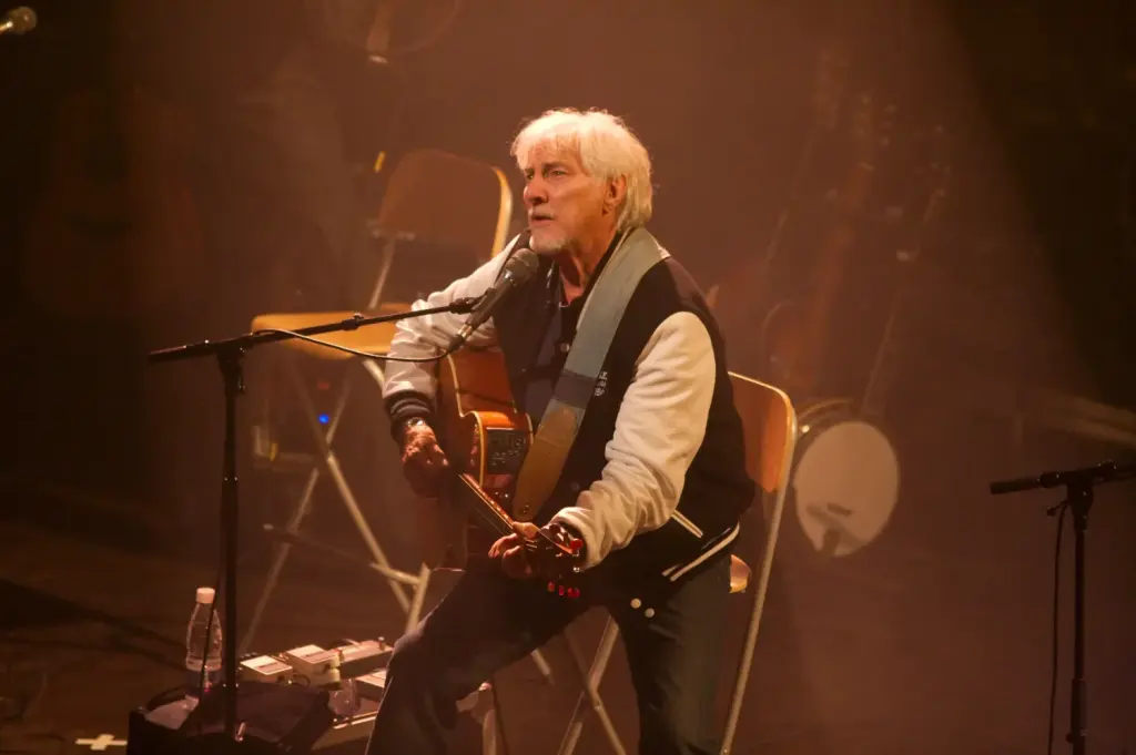 Hugues Aufray assis avec une guitare pendant un concert en 2009