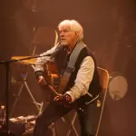 Hugues Aufray assis avec une guitare pendant un concert en 2009