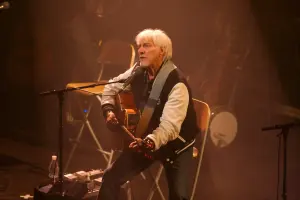 Hugues Aufray assis avec une guitare pendant un concert en 2009