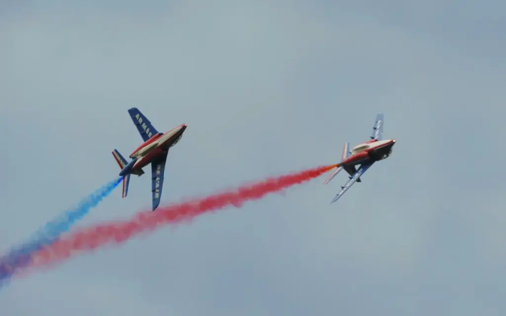 Deux Alpha Jet de la Patrouille de France en vol avec des fumées bleue et rouge.