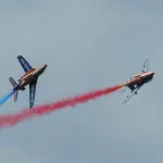 Deux Alpha Jet de la Patrouille de France en vol avec des fumées bleue et rouge.