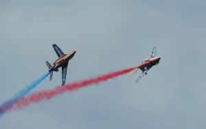 Deux Alpha Jet de la Patrouille de France en vol avec des fumées bleue et rouge.